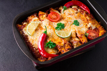 Mexican enchiladas with chicken, vegetables, corn, beans, tomato sauce and cheese. Served on a pan. Mexican food. Latin American cuisine. Black background, top view