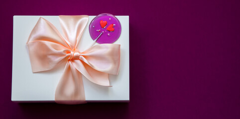 White gift box with bow and lollipop on a lilac background. Copy space