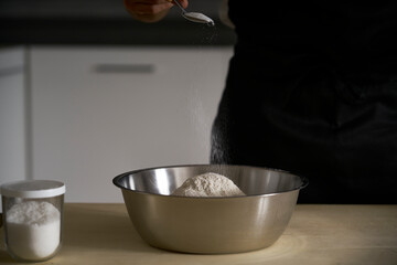 Human hands add salt and yeast to wholemeal flour dough to make bread, pasta, cake or pizza. The cook on the wooden table of his kitchen carries on the tradition of homemade pasta.