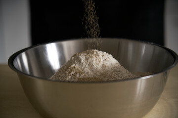 Human hands add salt and yeast to wholemeal flour dough to make bread, pasta, cake or pizza. The cook on the wooden table of his kitchen carries on the tradition of homemade pasta.