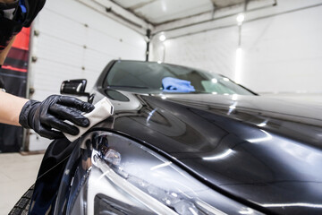 The process of applying a nano-ceramic coating on the car's hood by a male worker with a sponge and special chemical composition to protect the paint on the body from scratches, chips and damage.