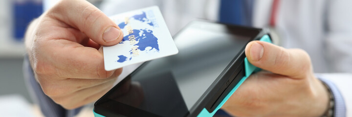 Close-up of adult person holding plastic credit card and machine in hands. Doctor in white uniform and red stethoscope. Online pay and remote transaction concept
