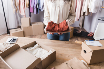 Cropped view of african american showroom owner holding clothes near boxes and cards with thank you lettering