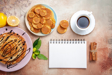 Overhead view of simple and decorated classic pancakes with fruits and notebook on colourful table