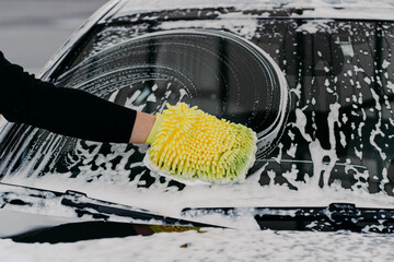 Car cleaning at self wash service. Mans hand with cloth washing cars windshied with foam soap. Auto...