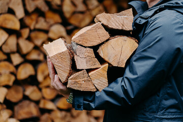 Close up of unrecognizable man dressed in jacket carries bundle of firewood, going to make fire...