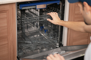 A man or service worker installs, disassembles, or performs maintenance on the dishwasher trays
