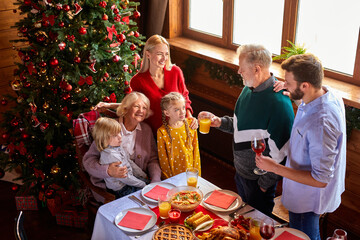 extended family congratulating, talking toasts behind christmas table. elderly man hold glass with beverage in hands and talk