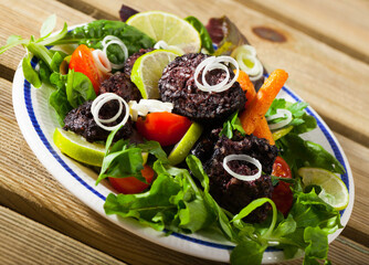 Image of fried tasty blood sausage with lettuce and lemon, served at plate