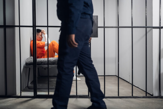A prison guard makes a tour of the cells in a high-security prison. The cells are occupied by criminals in red robes