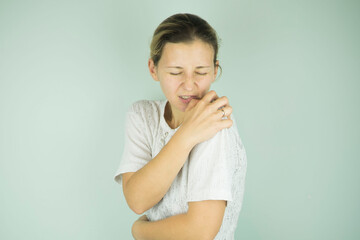 girl holding her shoulder in pain on gray background