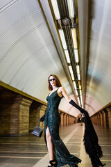 glamour woman in long black dress posing with handbag and faux fur jacket at subway station