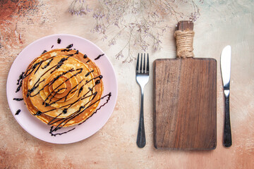 Stuffy pancakes decorated with chocolate syrup and fork and knife among cutting board