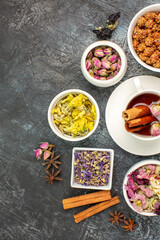 top view of a cup of herbal tea with a bowl of nut and different types of flower on grey ground