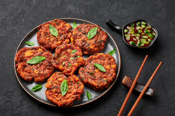 Tod Mun Pla or Thai Fish Cakes on black plate on dark slate table top. Traditional Thailand cuisine dish. Asian food and meal.