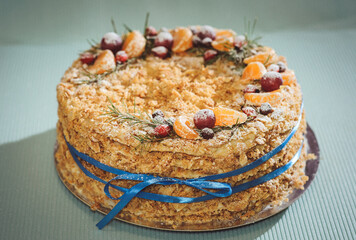 Napoleon's cake is decorated with New Year's composition consisting of pieces of mandarin, grapes, fir branches and brier. A leaf cake on a blue background is associated with a blue ribbon