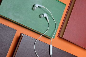 white vacuum headphones lie on books laid out on an orange background. audiobook concept.