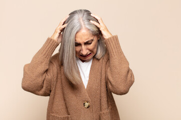 middle age woman feeling stressed and frustrated, raising hands to head, feeling tired, unhappy and...