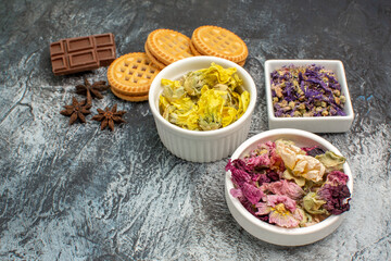 close up view of three bowls of dry flowers with chocolate and cookies on grey background