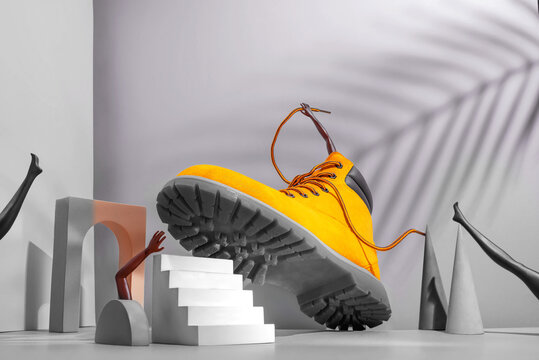 Shoe concept, yellow boots on the stairs, women's legs and hands, palm shade on gray background, arch and other geometric shapes.