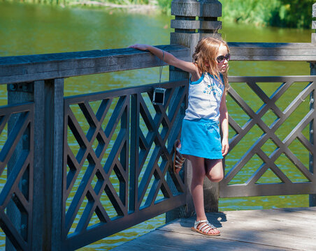 Little Girl Stands on a deck of a pond