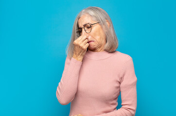 middle age woman feeling disgusted, holding nose to avoid smelling a foul and unpleasant stench