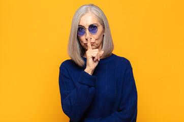 middle age woman looking serious and cross with finger pressed to lips demanding silence or quiet,...