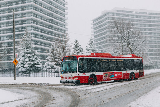 Toronto, Ontario, Canada - November 22, 2020: Toronto public transport TTC red bus during heavy winter snowstorm snowfall outdoors in city street. Snow blizzard and bad weather winter conditions.