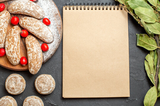 Delicious cookies on a cutting board with red cornell berries and notebook on dark background