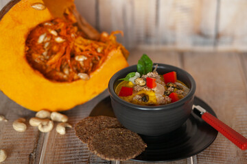 Pumpkin creamy soap in a black bowl, and ingredients blurred in the wooden background .