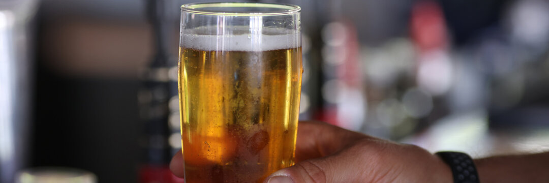 Hand holds glass with cold beer and froth. Rent of beer equipment concept