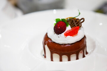 On a white plate, a small cake doused with chocolate glaze and decorated with berries.