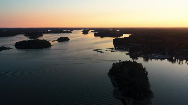 Aerial silhouette view of a boat arriving at a dock, sunrise, in the Scandinavia - reverse, drone shot
