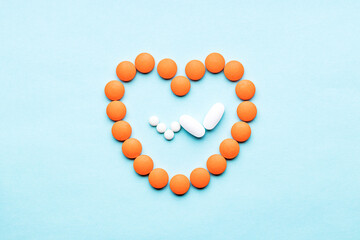 heart symbol formed orange pills and pulse trace inside isolated on a blue background. above view. outer space. cardiac medicine concept