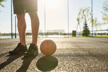 Close up of legs of young male basketball player in sportswear standing on the court with...