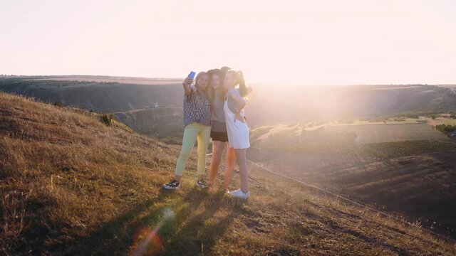 A group of three girls filming a video blog sitting on a cliff in the mountains, Charismatic Girls. Rocks in the background. One of the girls has a guitar behind her.