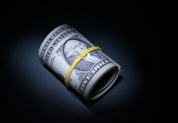 Several one-dollar bills are rolled up with a tube and tied with an elastic band, close-up. The dollar is in a low key.