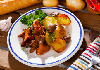 Fried chanterelles served with grilled chicken hearts and potatoes on white plate..