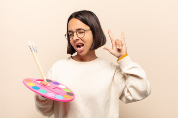 young hispanic woman feeling happy, fun, confident, positive and rebellious, making rock or heavy metal sign with hand