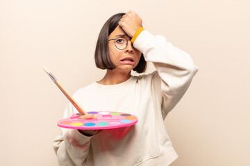 young hispanic woman raising palm to forehead thinking oops, after making a stupid mistake or...