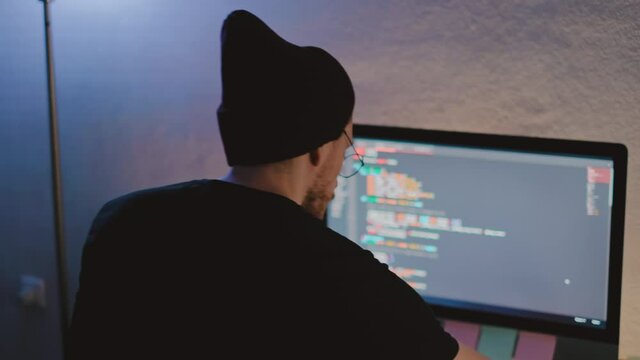 Young man mobile developer writes program code on a computer, programmer work in home office.