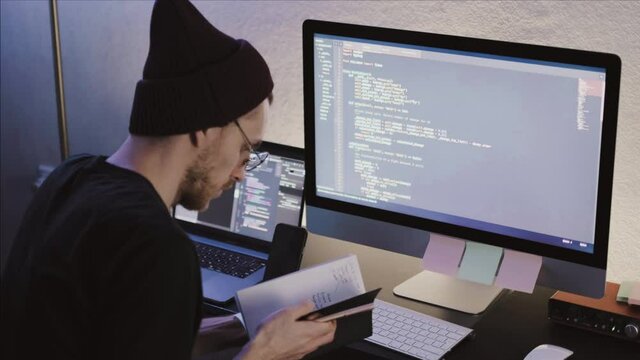 Young man mobile developer studying on a computer, taking notes. Programmer work in home office.