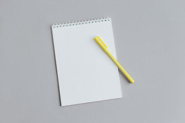 Notebook with blank page and yellow pen on a grey background.