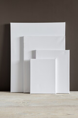 White blank canvases of various sizes stand against a dark wall. Mockup. Materials for painting with oil paints and acrylics. Close-up photo.