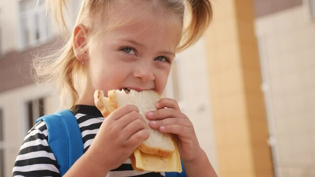 schoolgirl eating a sandwich during recess in school. kids education concept lifestyle. little girl kid schoolgirl with a backpack eating a sandwich. kid child is having lunch at school