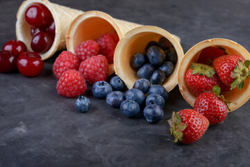 fresh berries  in waffle cones on black stone background