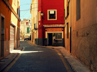 The colorful world of Spain. Red and yellow buildings. The street is going uphill. Blue sky.
