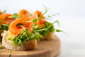 Canapes with mozzarella cheese, salad, salmon and pea sprouts, toast with red fish on a wooden board close up