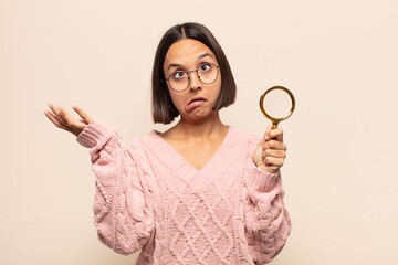 young hispanic woman shrugging with a dumb, crazy, confused, puzzled expression, feeling annoyed...