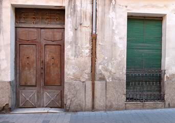 Two weathered doors, one painted green and one wood colored, one drain pipe. Everything is old and has clearly seen better times.